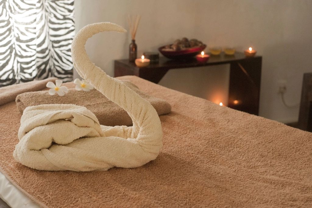A spa treatment bed with a towel folded into a swan and lit candles