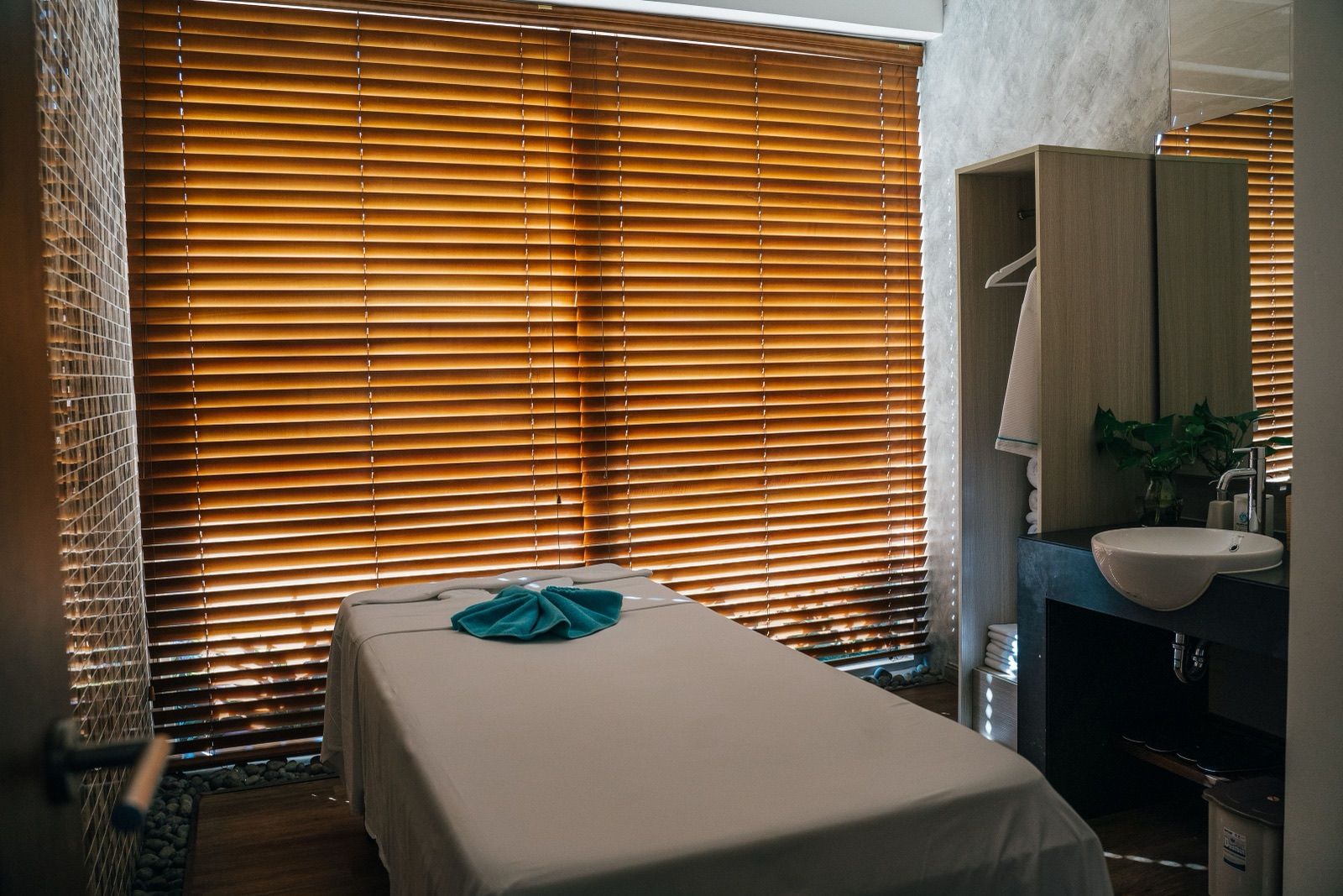 Quiet spa treatment room with a massage bed and warm wooden blinds