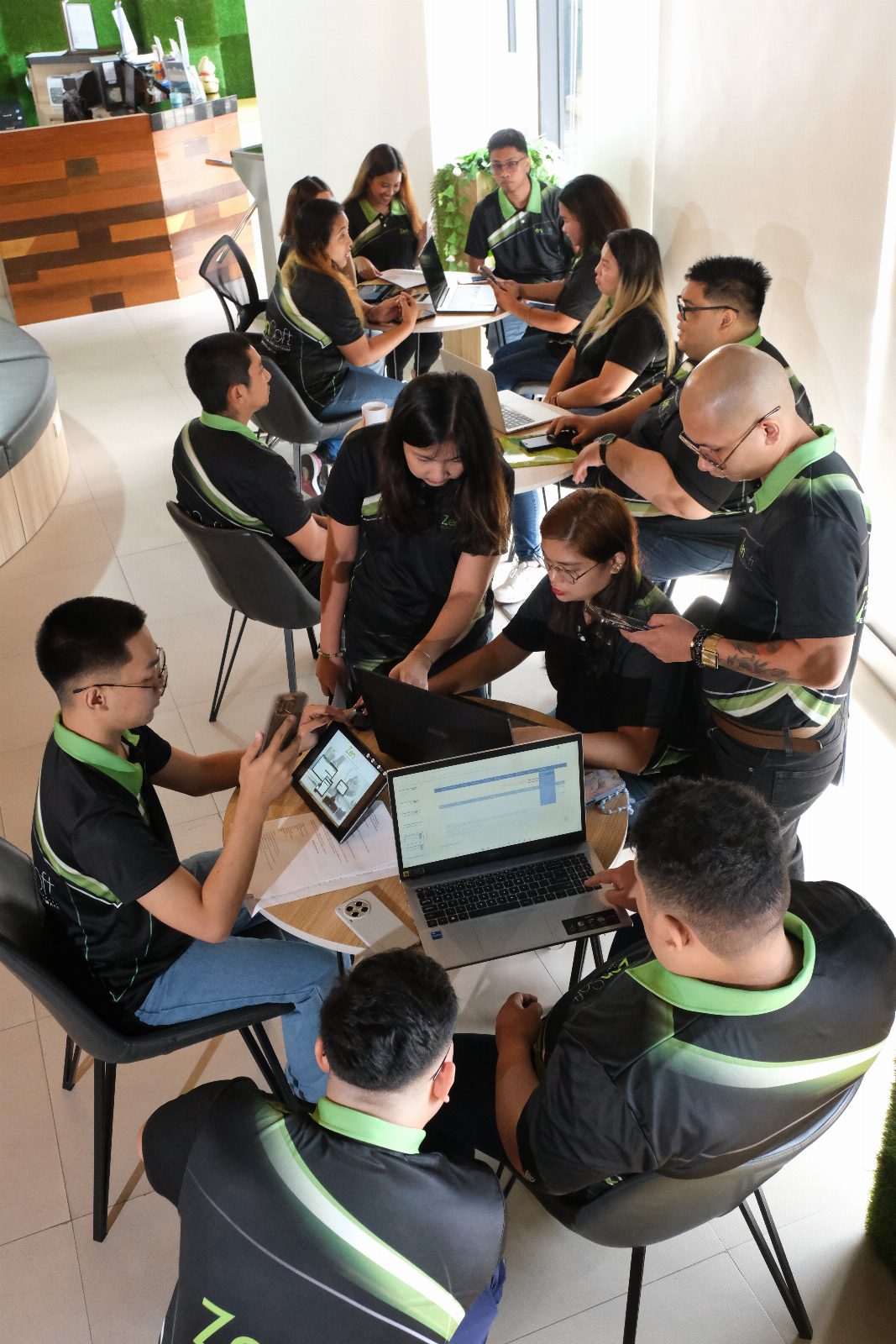 A high angle view of the ZenSoft team clustered around laptops at the lounge tables, working through a task together